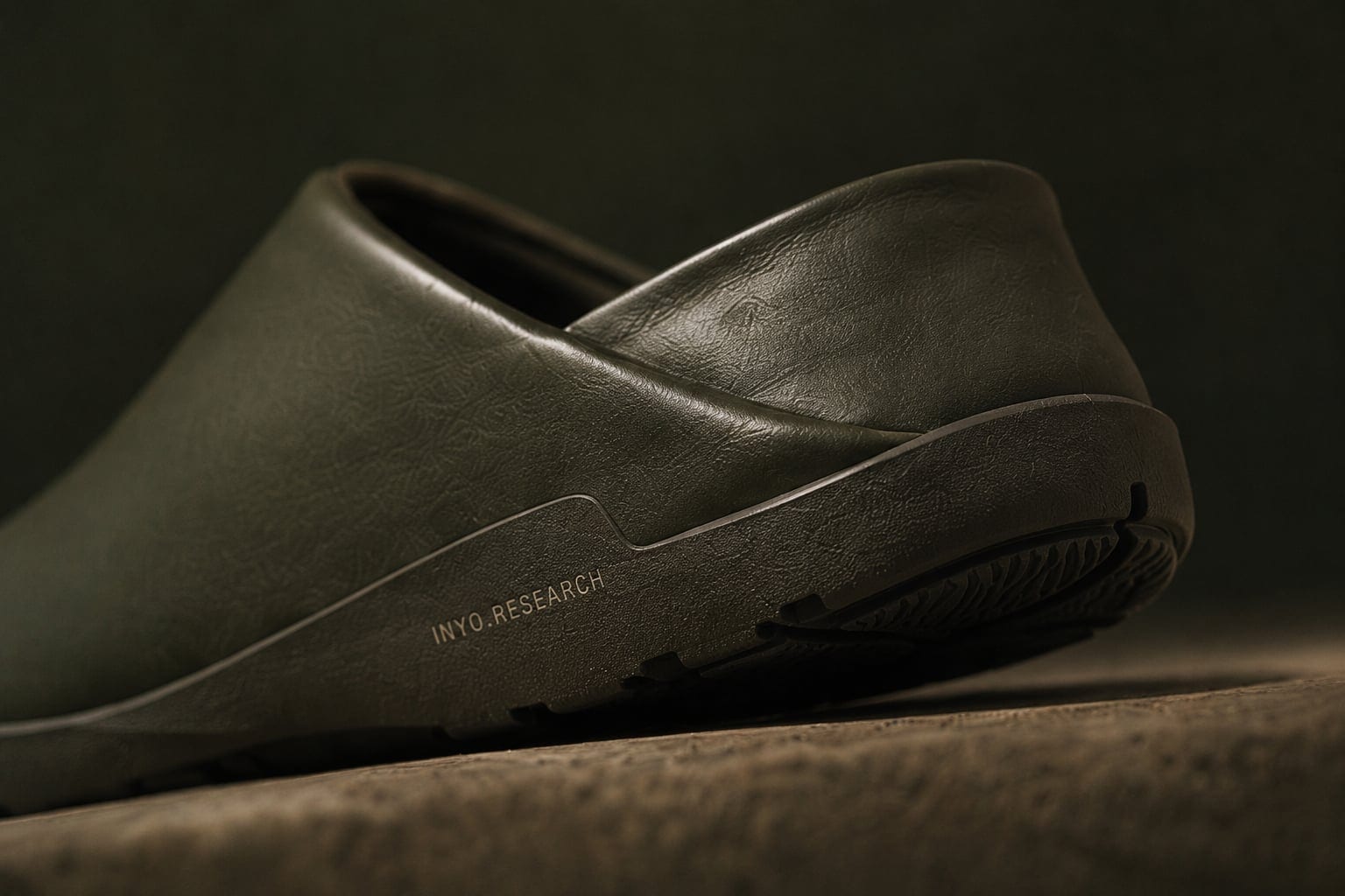Inyo olive leather mule, low three-quarter view in raking side light, on warm concrete.